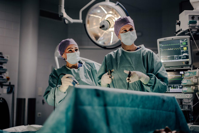 Kaksi gynekologia leikkaussalissa suorittamassa leikkausta robotin avulla. Molemmilla on yllään suojavaatteet ja taustalla leikkaussalivälineistöä.