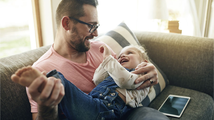 A child is laughing in her dad's lap.