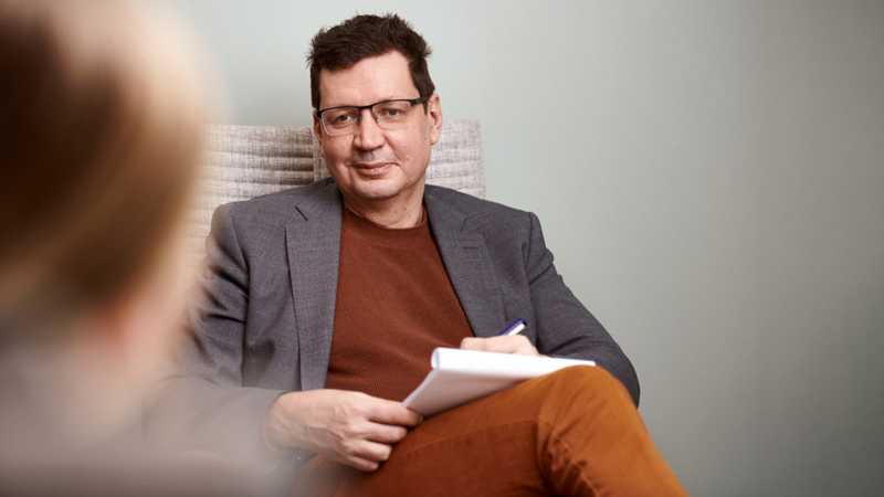 Psykiatri Sami Leppämäki istuu muistikirja kädessään. Potilas istuu häntä vastapäätä.